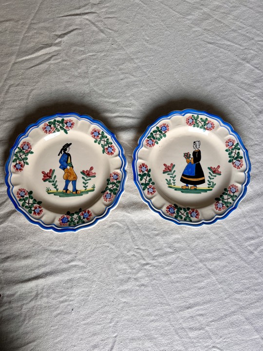 Two hand-painted faience plates with Breton figures, laid on linen